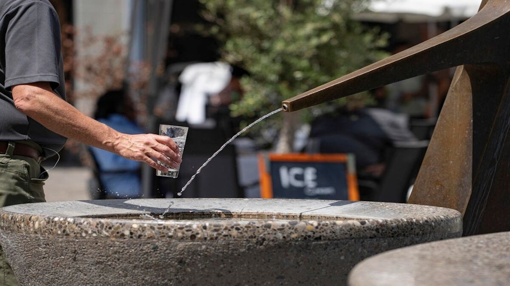 Person füllt Glas an einem Brunnen